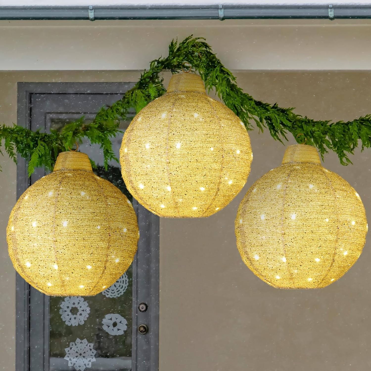Three illuminated spherical lanterns hanging against a neutral background with greenery.